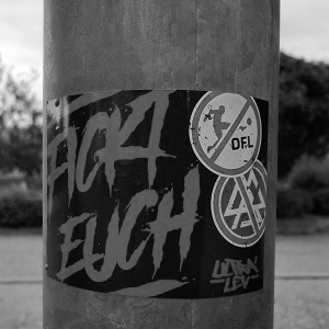 Dieser schwarzweiße Bildausschnitt von Thorsten Hülsberg zeigt einen Aufkleber auf einem Laternenmast mit einem klaren Statement zu DFL und DFB. 